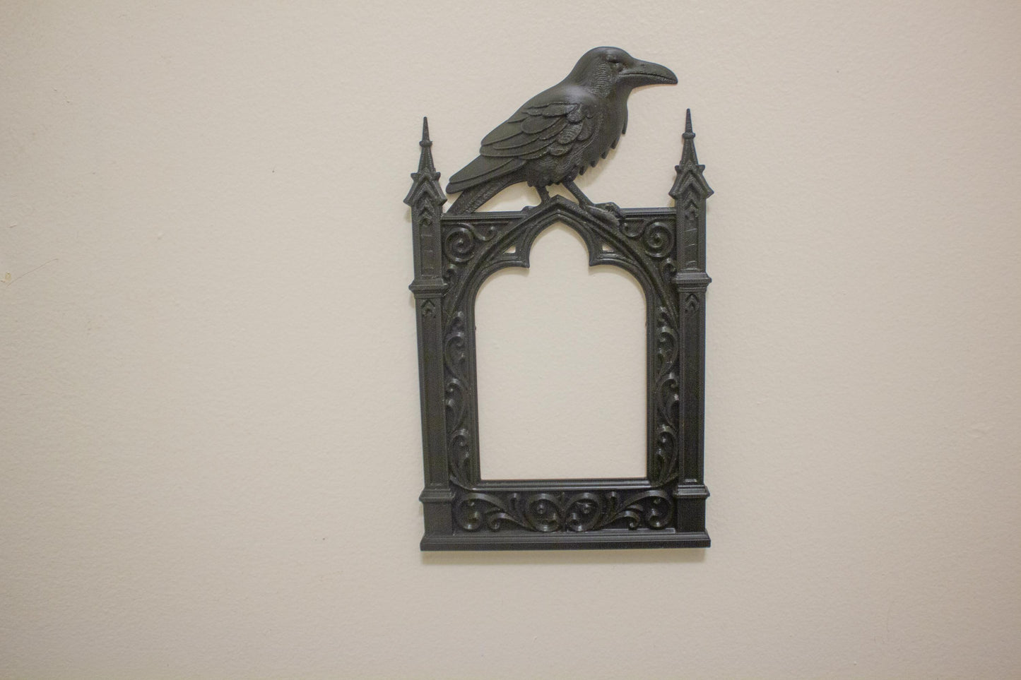 Decorative wall art with a crow on top of a gothic-style frame against a beige background