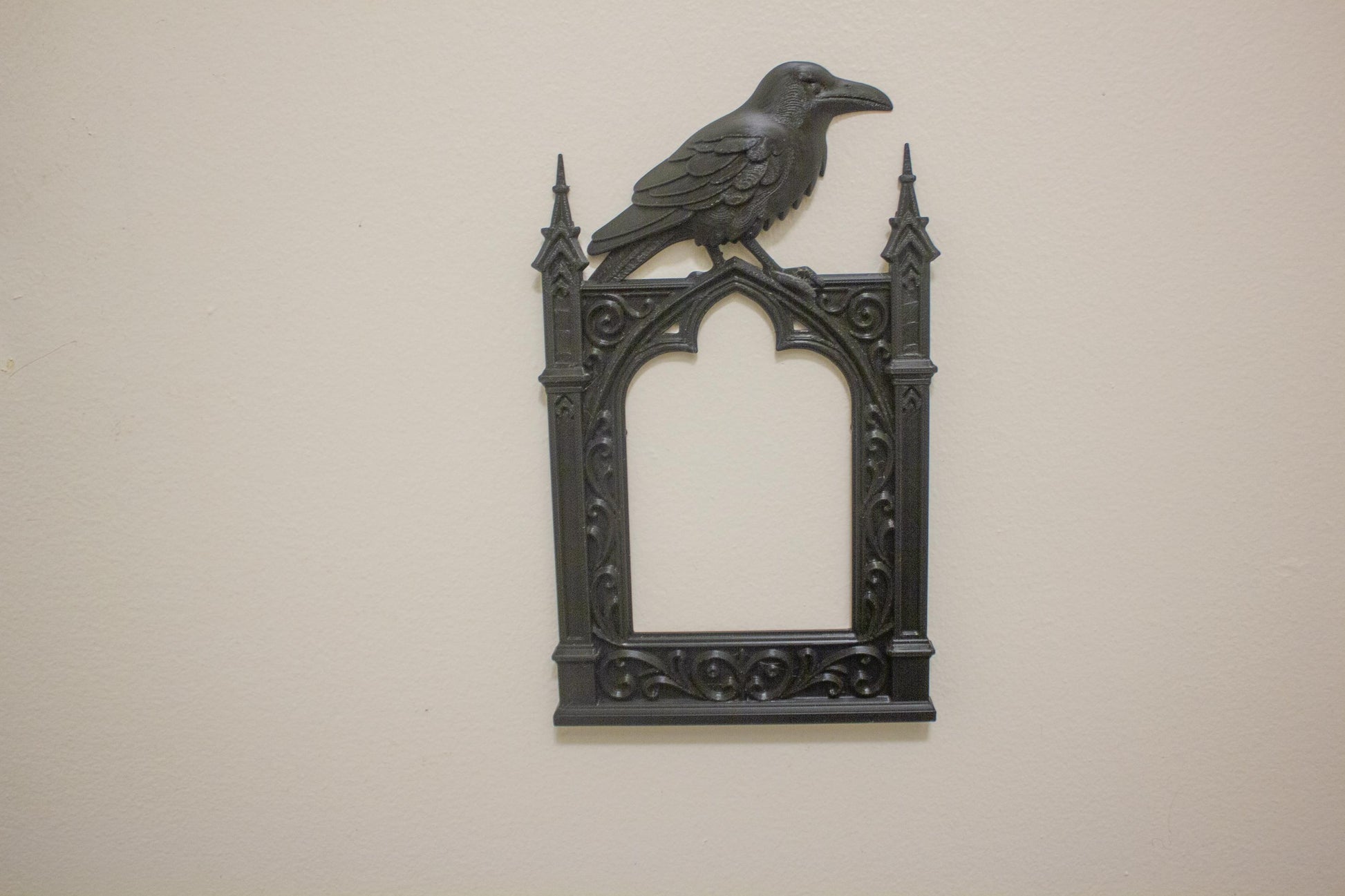 Decorative wall art with a crow on top of a gothic-style frame against a beige background