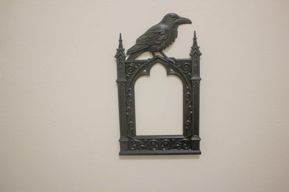 Decorative wall art with a crow on top of a gothic-style frame against a beige background